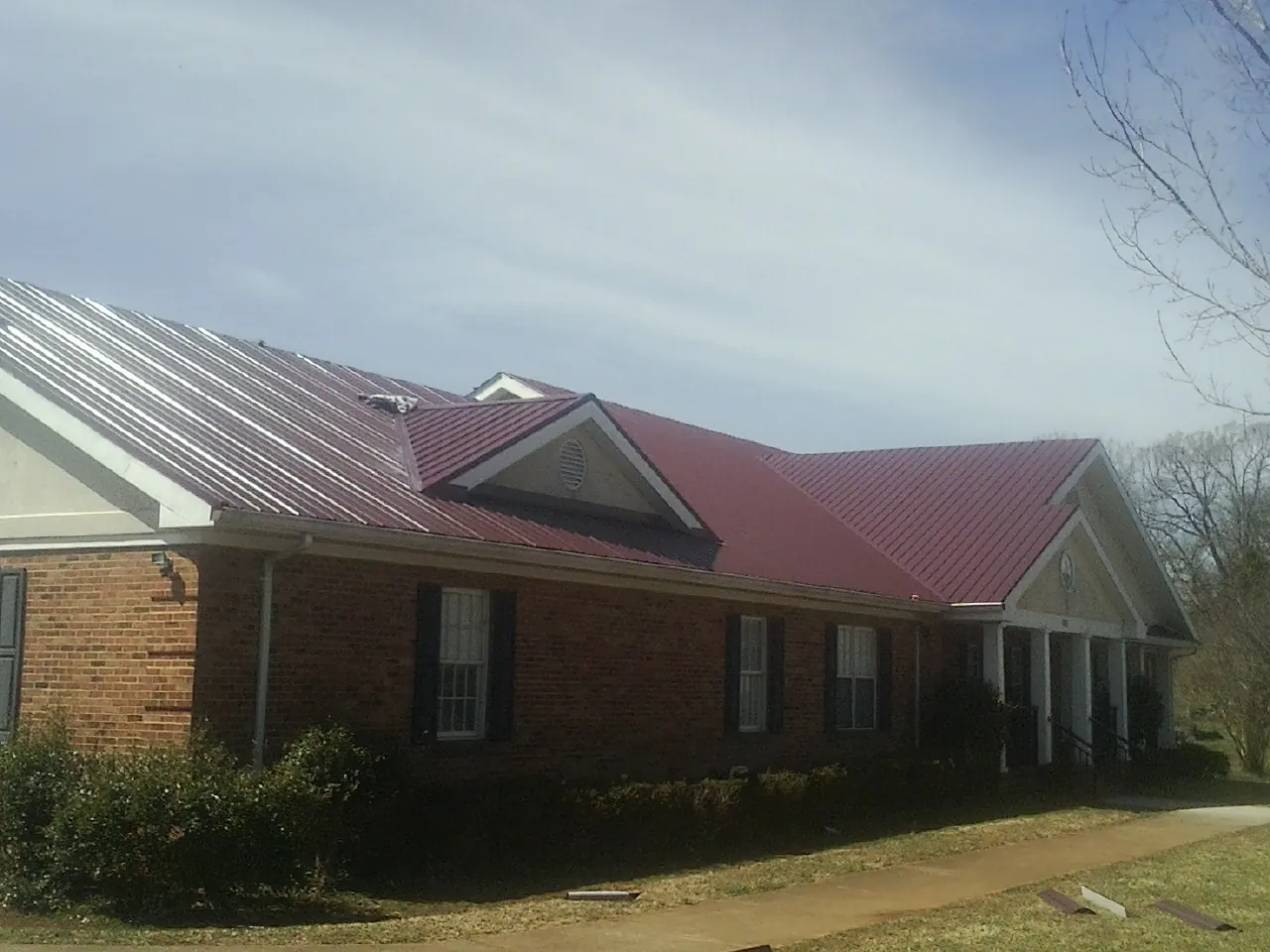 Red metal roof with gabled entries on a long brick building, from a Hail Damage Roof Repair job in Ballantine