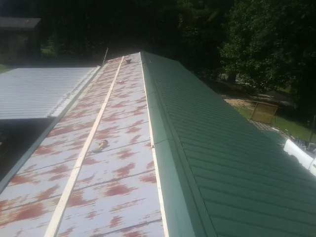 Old rusted panels beside newly installed green metal roofing — Wind Damage Roof Repair by Roofing Brothers in Ballantine