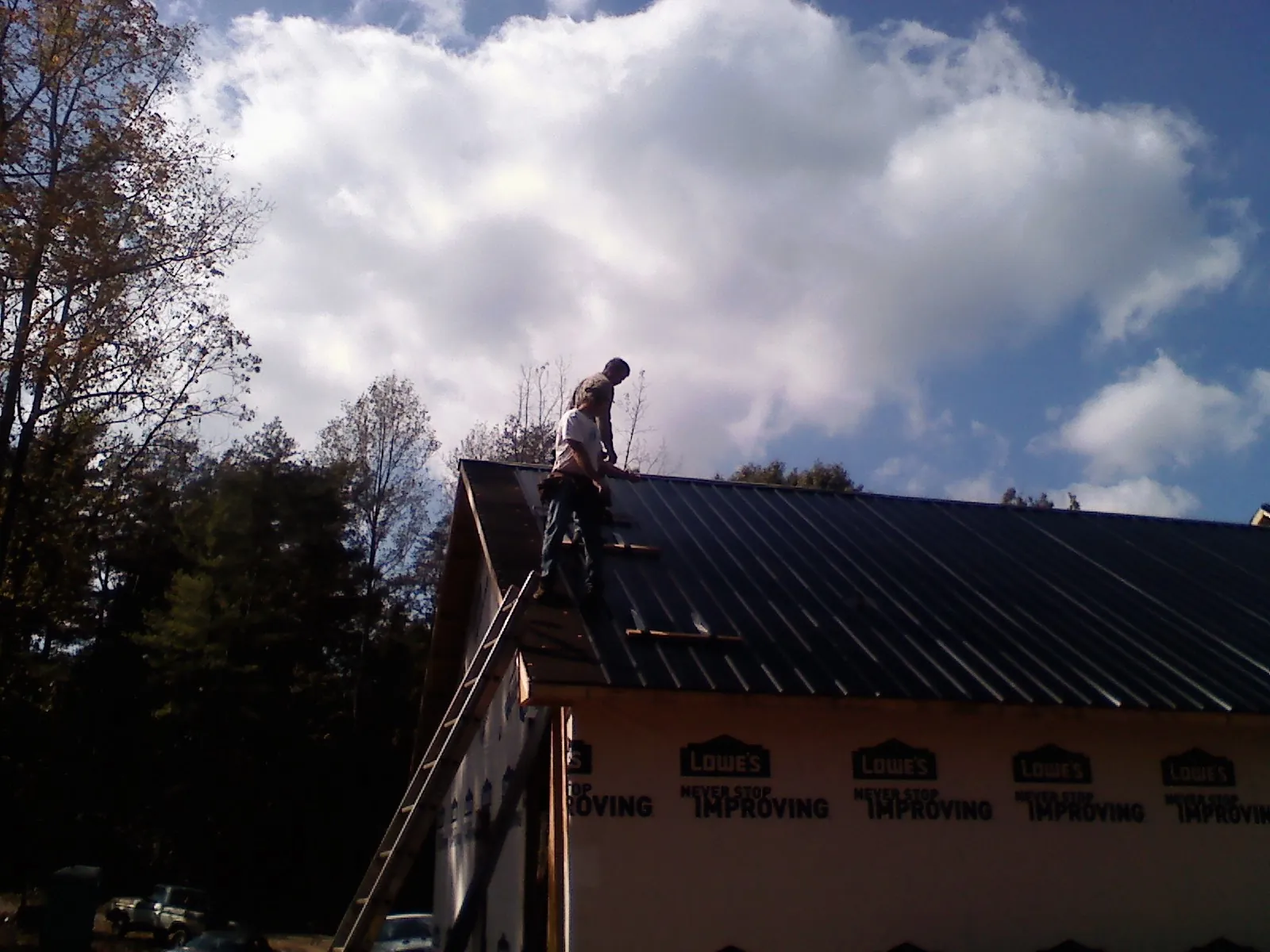 Roofer fastening dark metal panels high against a cloudy sky, from a Roof Inspection job in Ballantine