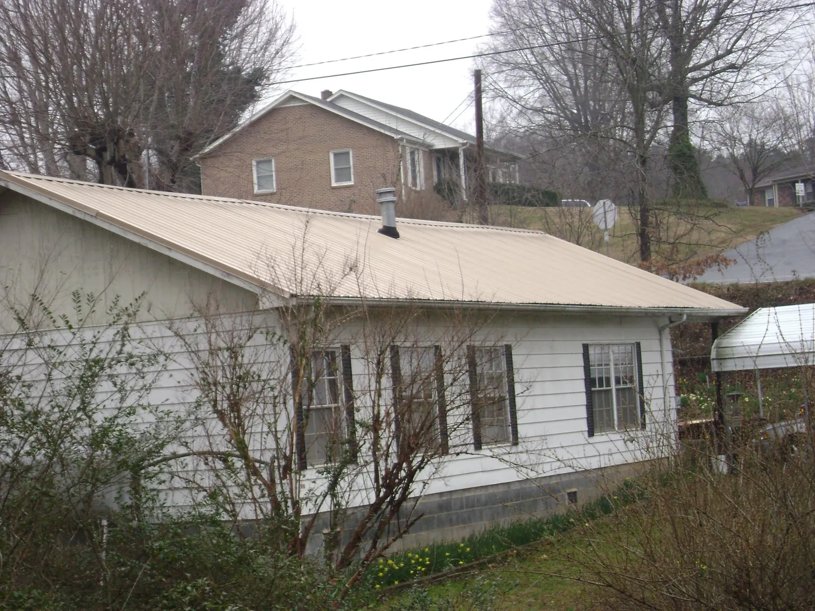 Tan metal roof on a white sided house set into a hillside — Commercial Roofing by Roofing Brothers in Ballantine